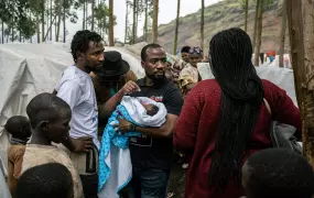 A man surrounded by people holds a baby in his arms. 